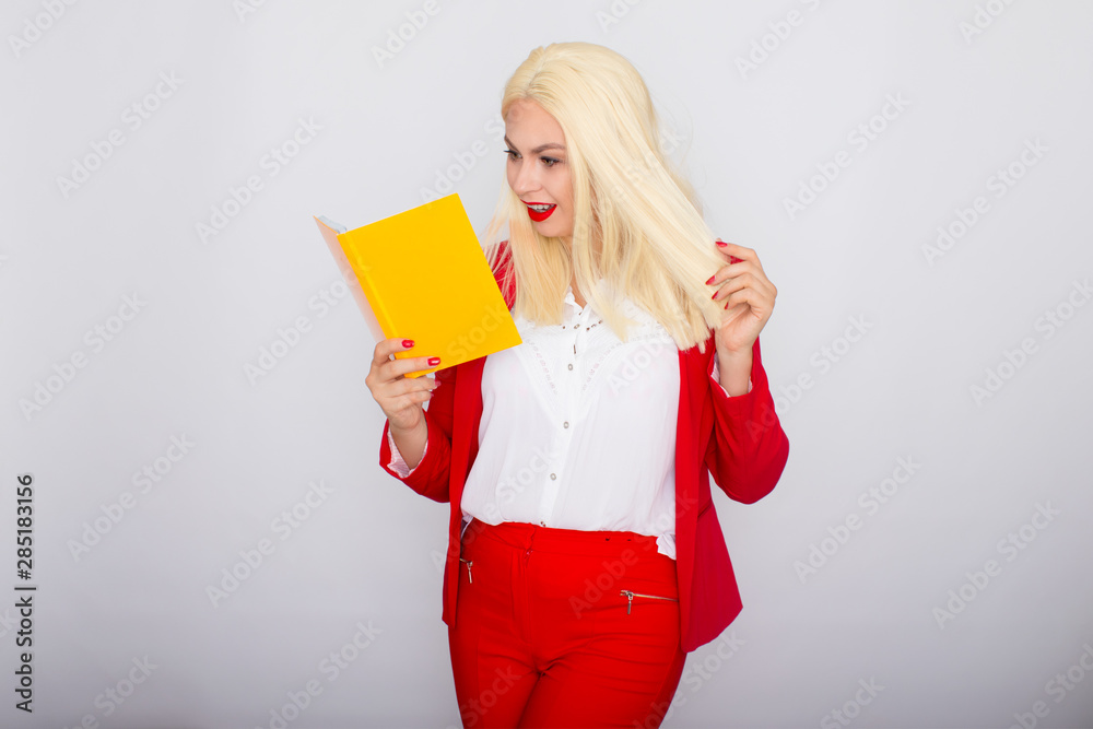 Attractive blonde haired woman wearing red jacket and pants, holding book in her hands Attractive blonde haired woman wearing red jacket and pants, holding book in her hands
