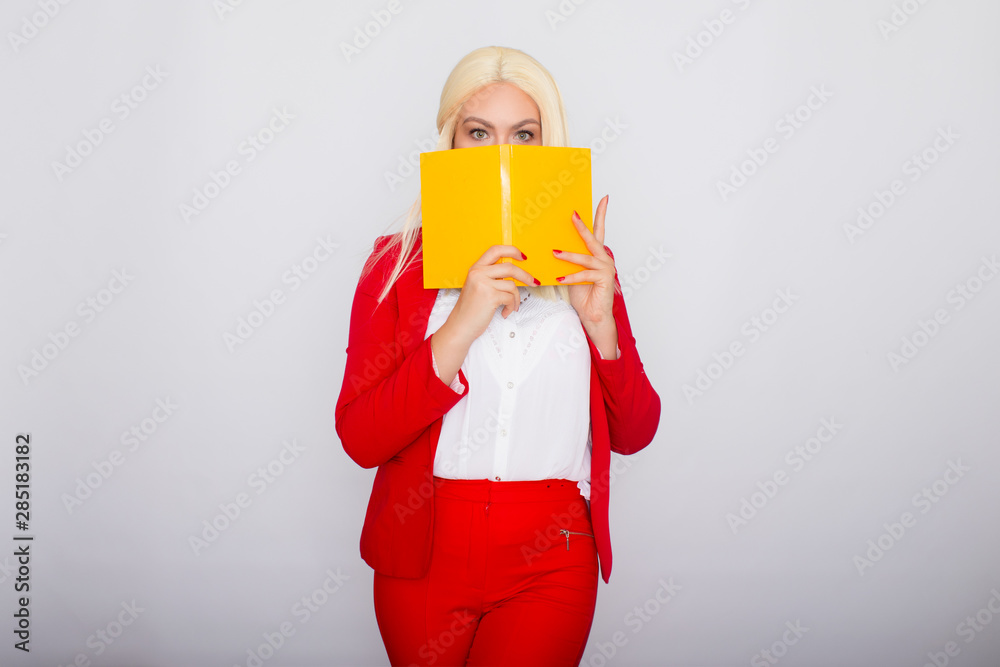 Attractive blonde haired woman wearing red jacket and pants, holding book in her hands Attractive blonde haired woman wearing red jacket and pants, holding book in her hands