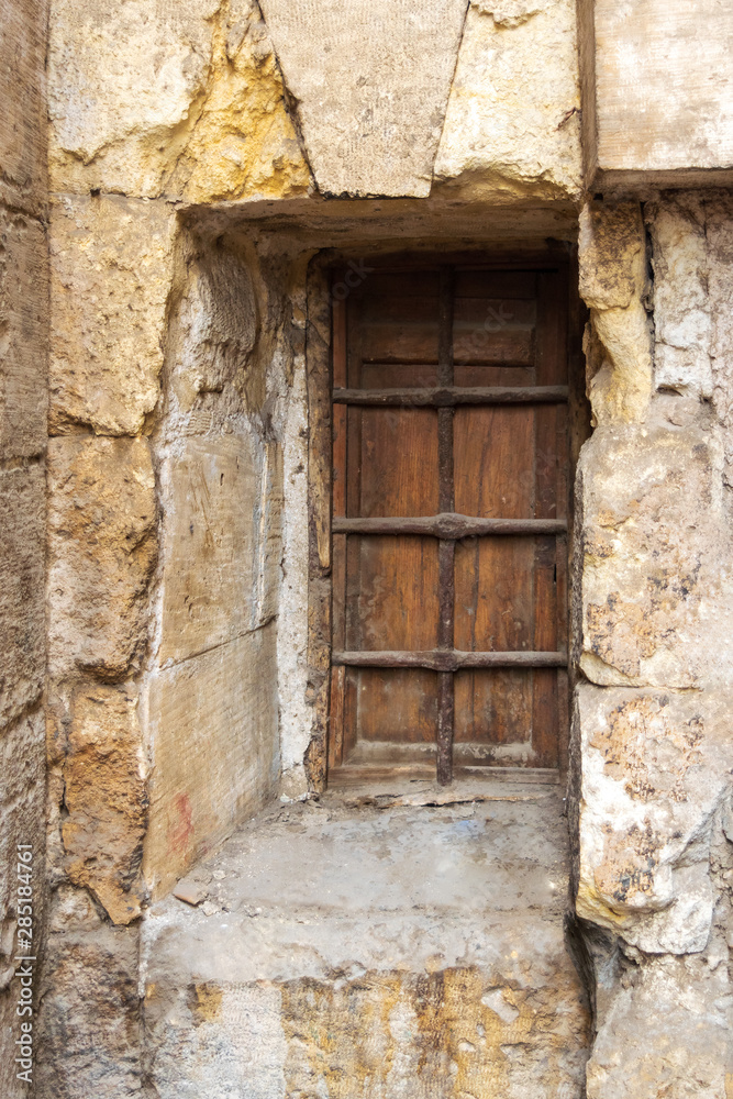 Wooden grunge closed window with wrought iron grid in stone bricks wall, Old Cairo, Egypt