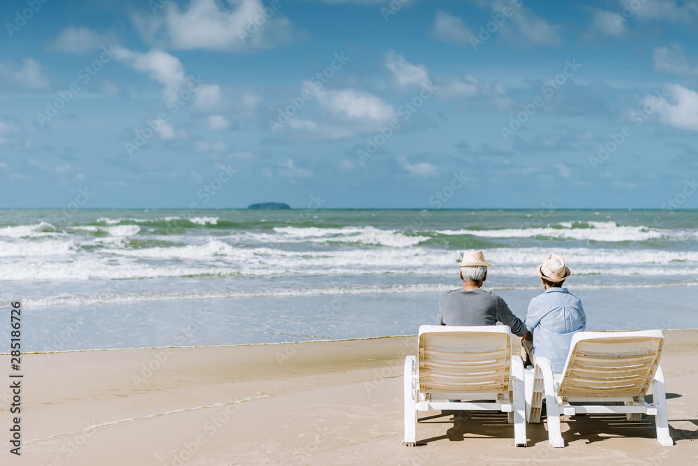 Asian senior couple or elderly people walking and siting at the beach on their weekend vacation holiday. Retirement vaction concept.