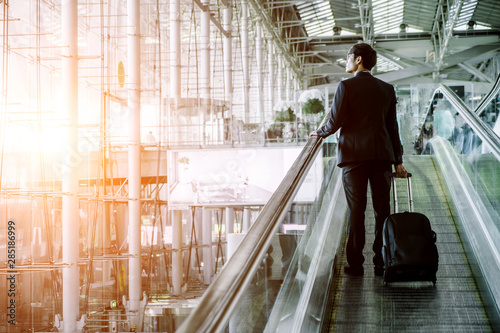 Elegant asian businessman checking email on mobile phone while walking with suitcase inside airport, experienced male employer using cell telephone while waiting for taxi car coming before work travel