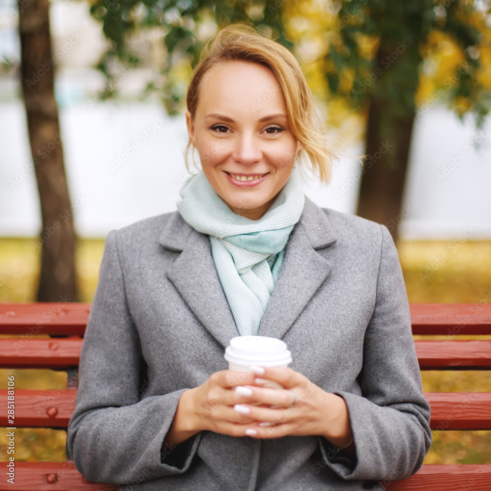 Cheerful pretty woman holding paper cup of coffee in autumn park