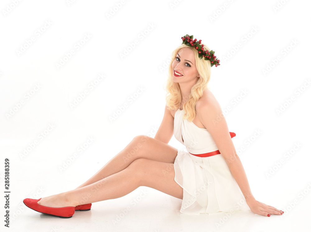 Naklejka premium full length portrait of blonde girl wearing a white dress and flower crown. Sitting pose, isolated against a white studio background.