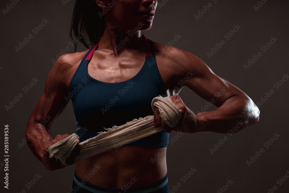 Close up of athletic healthy lean tone top body of asian woman holding white strap with both hands preparing for training or boxing while looking sideway with dark background.