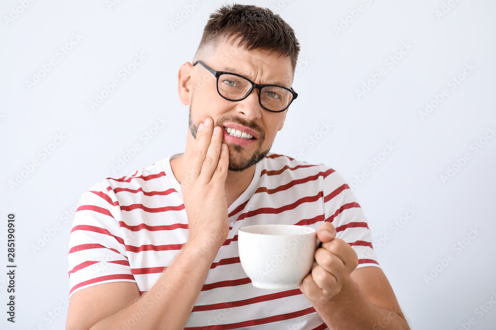 Man with sensitive teeth and hot coffee on light background Man with sensitive teeth and hot coffee on light background