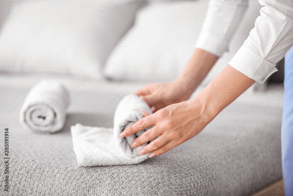 Female housekeeper rolling clean towel on bed