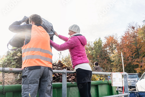 Woman and man giving waste green in container on recycling center
