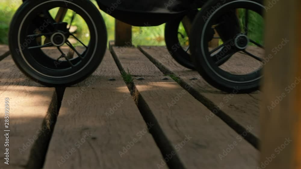 Woman with stroller crossing wooden bridge, close up shot Woman with stroller crossing wooden bridge, close up shot
