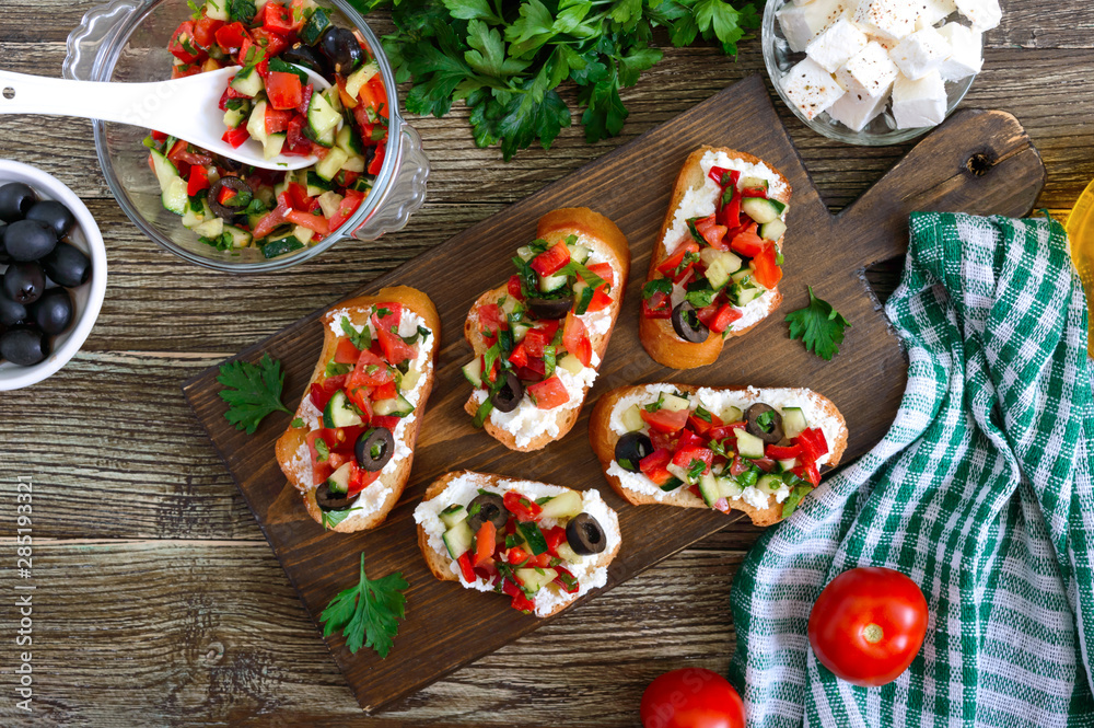 Delicious bruschettas with goat cheese and fresh vegetables. Crispy baguette slices with feta, tomatoes, cucumbers, peppers, olives, herbs. Healthy breakfast. Top view Delicious bruschettas with goat cheese and fresh vegetables. Crispy baguette slices with feta, tomatoes, cucumbers, peppers, olives, herbs. Healthy breakfast. Top view