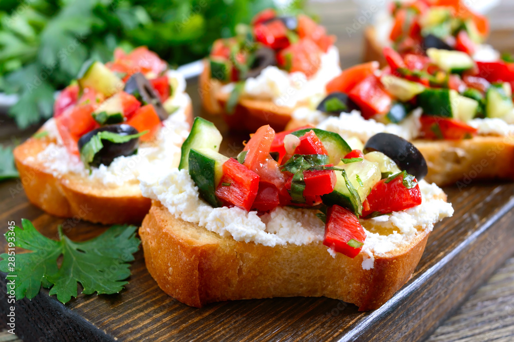 Delicious bruschettas with goat cheese and fresh vegetables. Crispy baguette slices with feta, tomatoes, cucumbers, peppers, olives, herbs. Healthy breakfast.