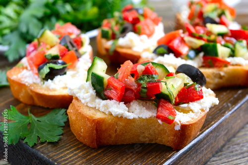 Delicious bruschettas with goat cheese and fresh vegetables. Crispy baguette slices with feta, tomatoes, cucumbers, peppers, olives, herbs. Healthy breakfast.