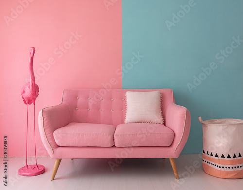 The pink sofa which has a white pillow is set in living room which has blue and pink wall.