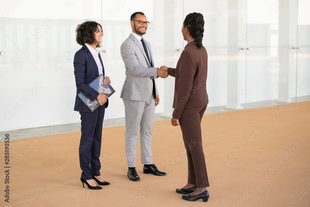 Fototapeta premium Happy business partners greeting each other in office hallway. Multiethnic business man and women standing and shaking hands. Partnership concept
