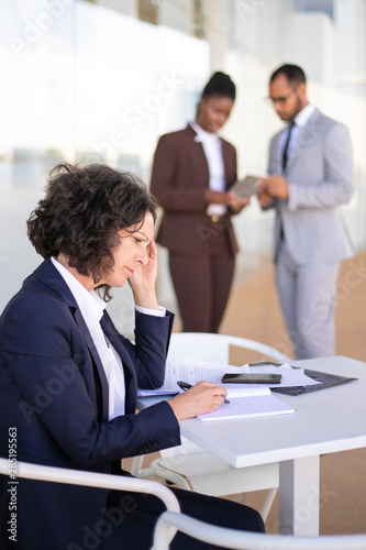 Upset stressed female employee working with papers. Tired businesswoman sitting at table with documents and reading notes. Fatigue or headache concept