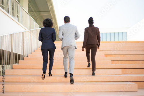 Businesspeople walking near office building. Rear view of business man and women going upstairs together. Businesspeople outside concept