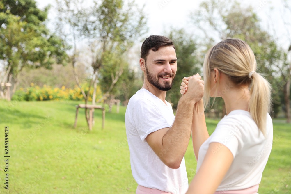 image of young caucasian couple in white and pink sport dress with smiling and arm wrestling challenge in the park with green tree in nature
