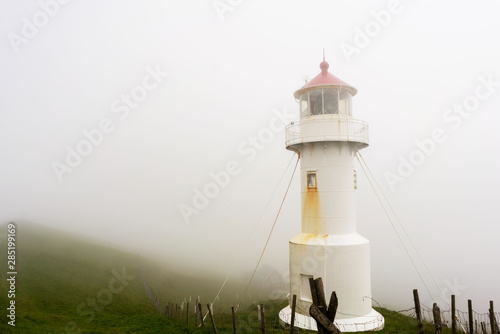 Lighthouse building on Mykines island covered with thick fog. Faroe Islands. © juhrozian