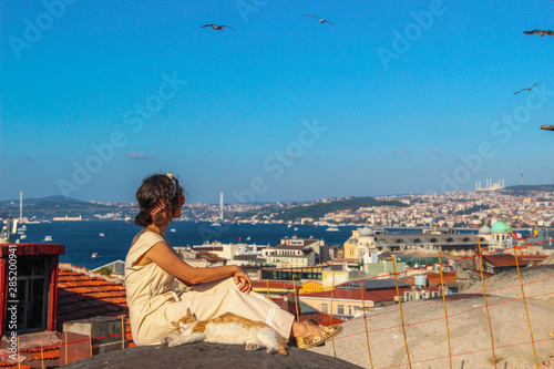 Fototapeta Naklejka Na Ścianę i Meble -  Woman touching yellow cat at the roof with bosphorus background in Istanbul