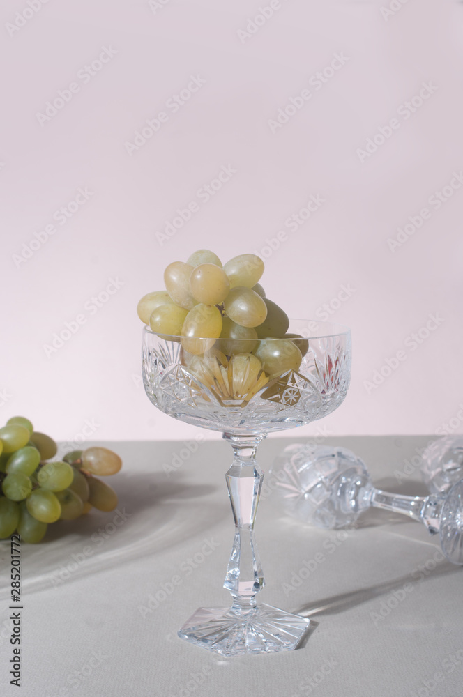 Minimalistic grapes in crystal glasses on light pink background Minimalistic grapes in crystal glasses on light pink background