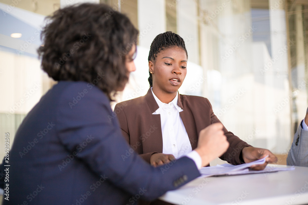 Confident female professional explaining document details to colleagues Multiethnic business man and women sitting at table and checking papers. Paperwork concept
