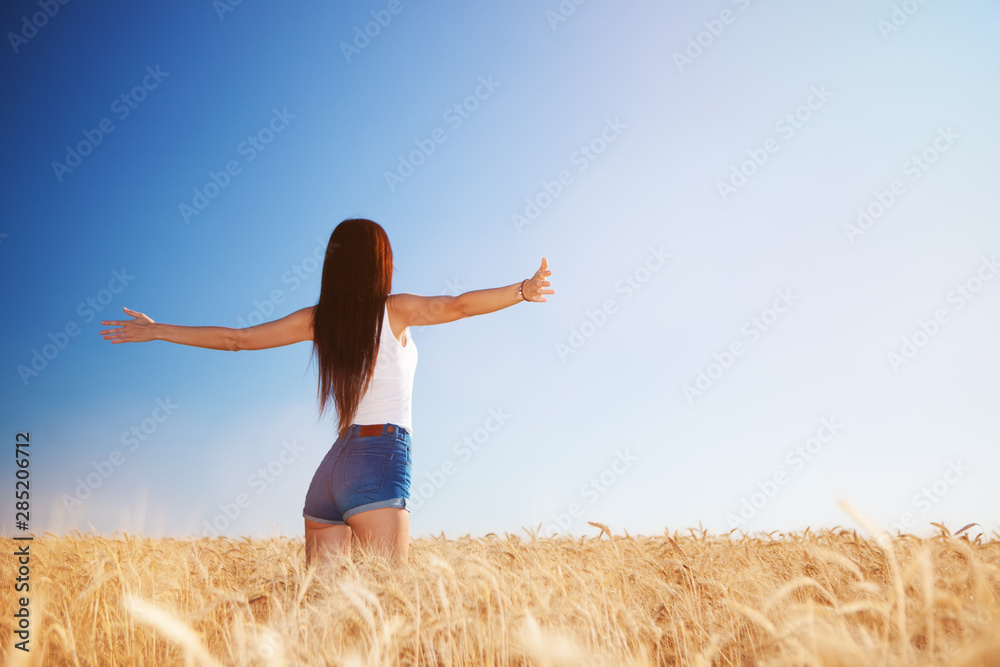 Happy woman enjoying the life in the field. Nature beauty, blue sky,white clouds and field with golden wheat. Outdoor lifestyle. Freedom concept. Woman jump in summer field