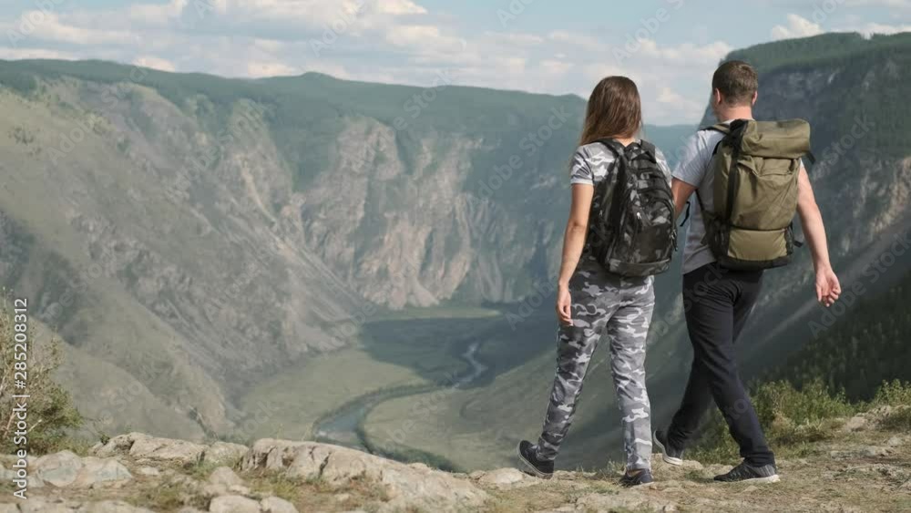 Male and female travelers approach the peak of the mountain and rejoice at success raising their hands up Male and female travelers approach the peak of the mountain and rejoice at success raising their hands up