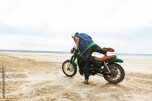Fototapeta Naklejka Na Ścianę i Meble -  Handsome man biker on his bike outdoors on a beach in helmet.