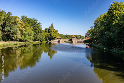 View from the river "Weisse Elster" in Leipzig with trees, bridges and a weir at blue sky