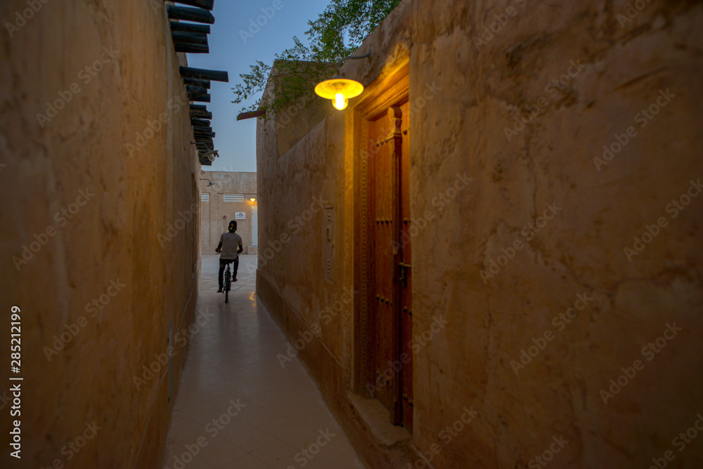 Unidentifiable man riding a bicycle in a narrow passageway of Souq Wakrah, Qatar