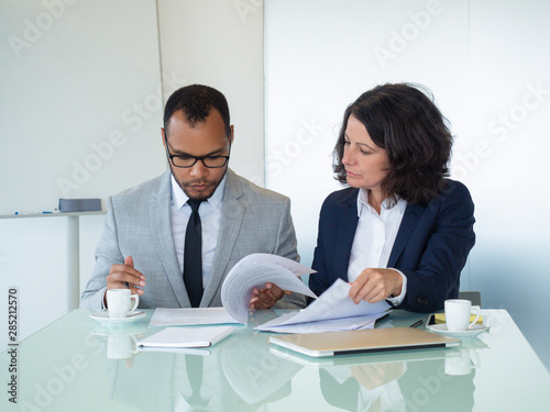 Business colleagues checking agreement text. Business man and woman sitting at meeting table and reading documents together. Teamwork concept