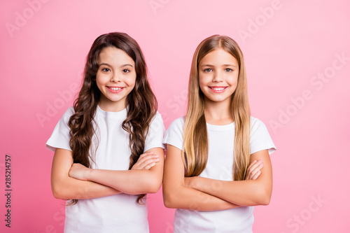 Photo of two nice good friendly girls with their hands folded staring at camera while isolated with pink background