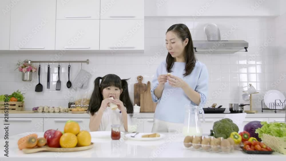 Happy Asian family Mother and Little girl are eating breakfast in the kitchen at home. Bread with jam and drinking milk. Healthy food concept Happy Asian family Mother and Little girl are eating breakfast in the kitchen at home. Bread with jam and drinking milk. Healthy food concept