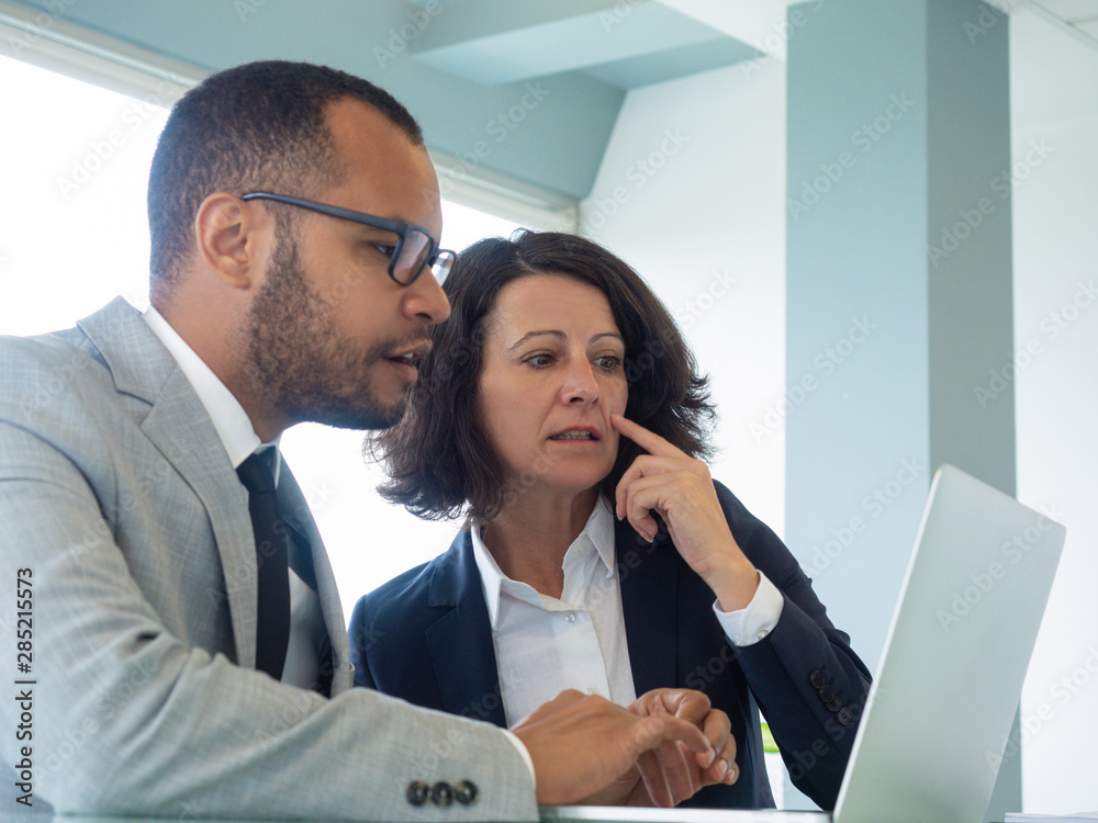 Excited professionals watching presentation on laptop. Business man and woman sitting at computer in meeting room and staring at screen. Business team or communication concept Excited professionals watching presentation on laptop. Business man and woman sitting at computer in meeting room and staring at screen. Business team or communication concept