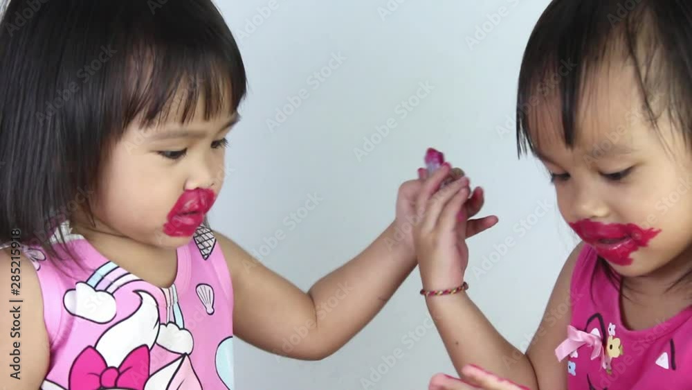 Happy Asian child girl with her sister apply red lipstick on lips and make kiss to camera. Happy Asian child girl with her sister apply red lipstick on lips and make kiss to camera.