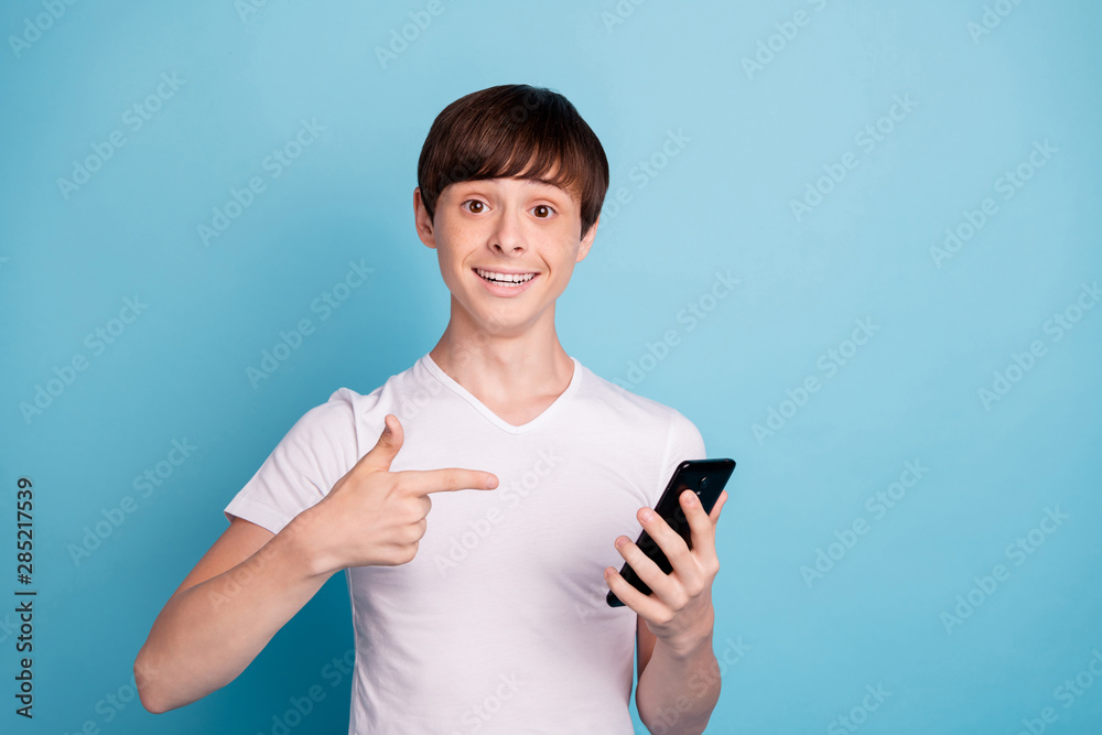 Photo of boy having been told to sell phone he is pointing at while isolated with blue background Photo of boy having been told to sell phone he is pointing at while isolated with blue background