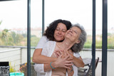 Happy mother and daughter with closed eyes hugging. Cheerful senior mother with adult daughter standing together and hugging at home. Family concept
