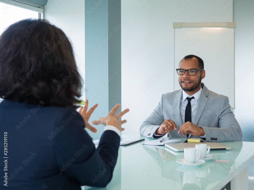 Obraz premium Excited male employer interviewing female applicant. Business man and woman sitting at conference table opposite of each other and talking. Career concept
