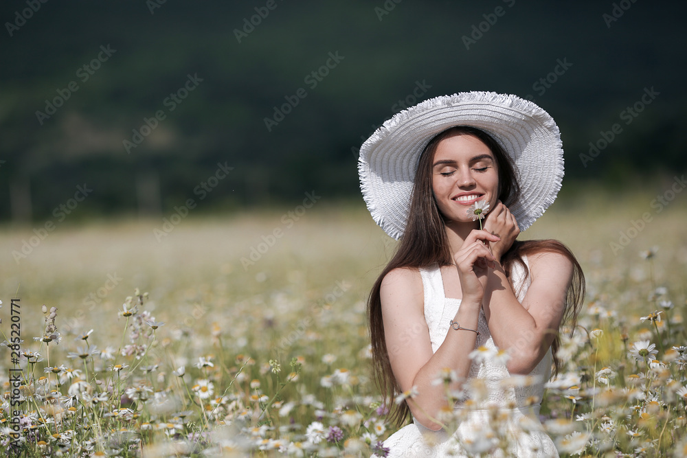 Fototapeta premium Beautiful girl outdoors with a bouquet of flowers in a field of white daisies,enjoying nature. Beautiful Model with long hair in white dress having fun on summer Field with blooming flowers,Sun Light.