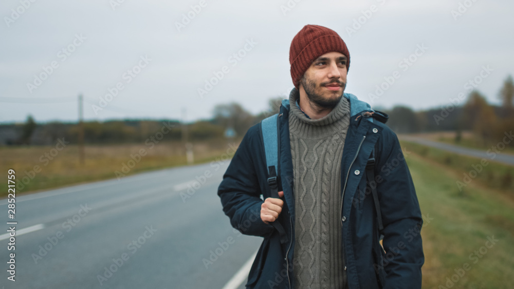 Casualy Dressed Hitchhiker Traveler Sitting by the Highway at a Cloudy Day. Casualy Dressed Hitchhiker Traveler Sitting by the Highway at a Cloudy Day.