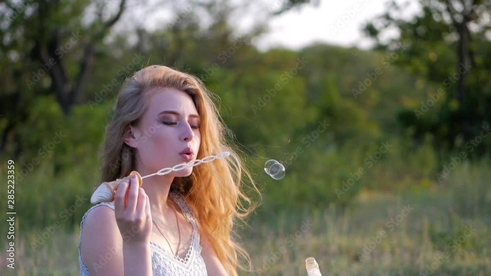 Young pretty woman on a green meadow blowing bubbles