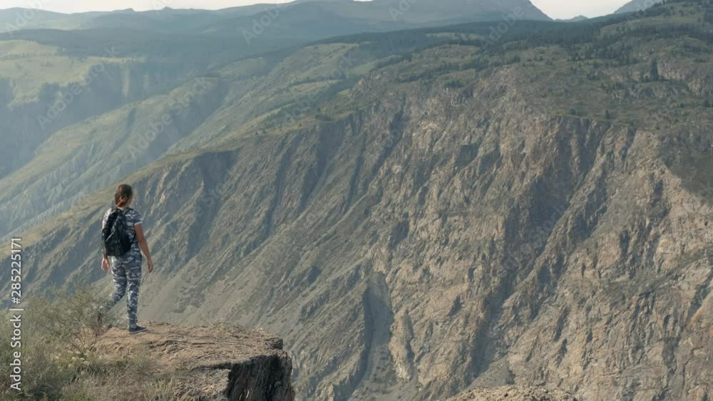 Girl tourist comes to the edge of the cliff having achieved success looking forward. Overall plan Girl tourist comes to the edge of the cliff having achieved success looking forward. Overall plan