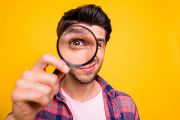 Photo of amazed man trying to see microorganisms with loupe but he evidently cannot manage to do it while isolated with yellow background