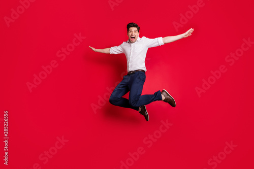 Full length body size photo of cheerful ecstatic man imagining he is airplane flying while isolated with red background