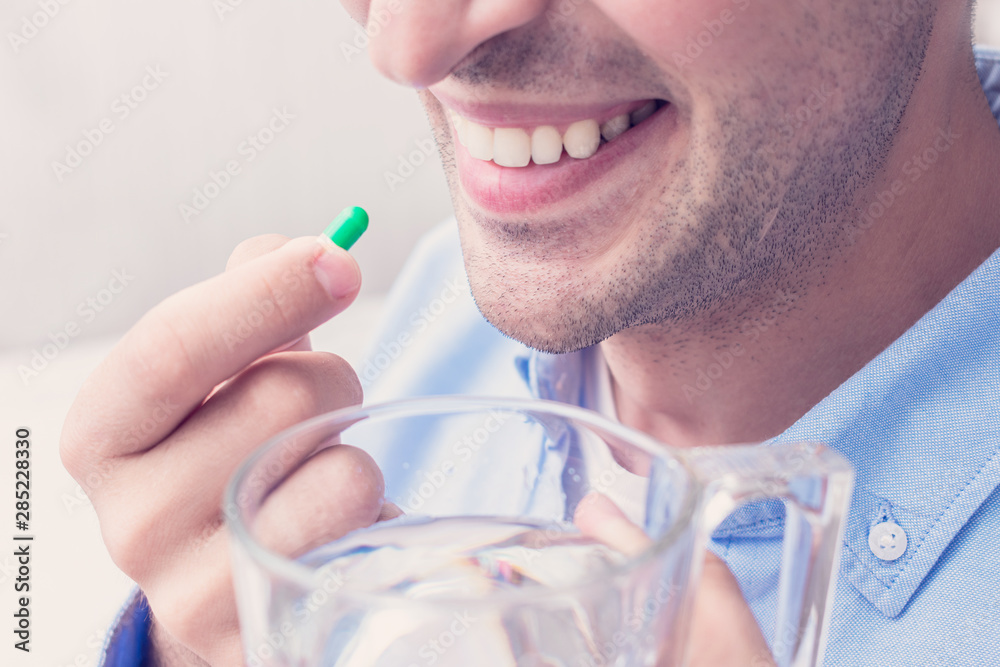 A young attractive man takes vitamins, capsule and glass of water, close up, cropped image, toned A young attractive man takes vitamins, capsule and glass of water, close up, cropped image, toned