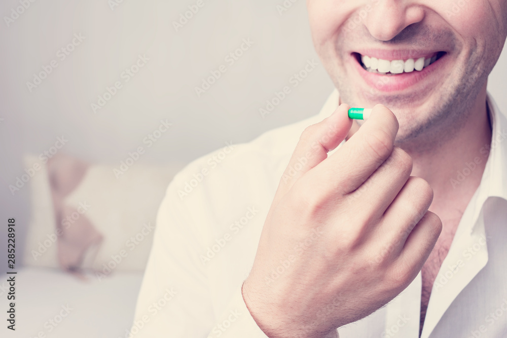 A young man takes vitamins or medication, the hand with the capsule, close up, cropped image, toned A young man takes vitamins or medication, the hand with the capsule, close up, cropped image, toned