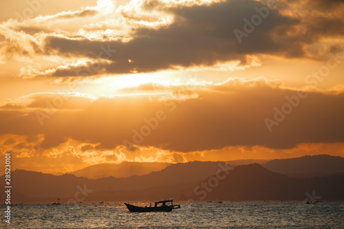 Lonely boat in the ocean by unset with mountains in the horizon. Sunset Over Lombok Island, Indonesia © Yevhenii