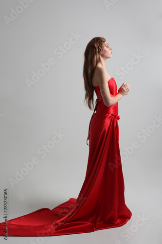 full length portrait of a  girl wearing a long red silk gown, Standing pose on a grey studio background.