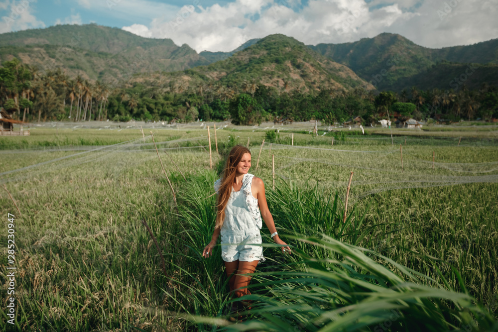 Relaxed healthy woman enjoying in pure nature at beautiful green rice fields on Bali. Concept of traveling, healthy and clean environment, ecology, balance in life, freedom, happiness, and well being