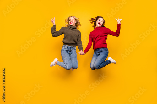 Full body photo of cute ladies jumping high showing v-signs wear knitted pullovers isolated yellow background