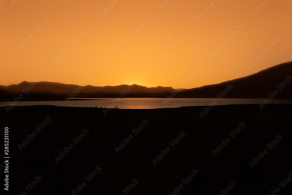 As the sun dips below the horizon, it casts a beautiful orange glow across the landscape and reflects on Lake Moogerah in Queensland, Australia